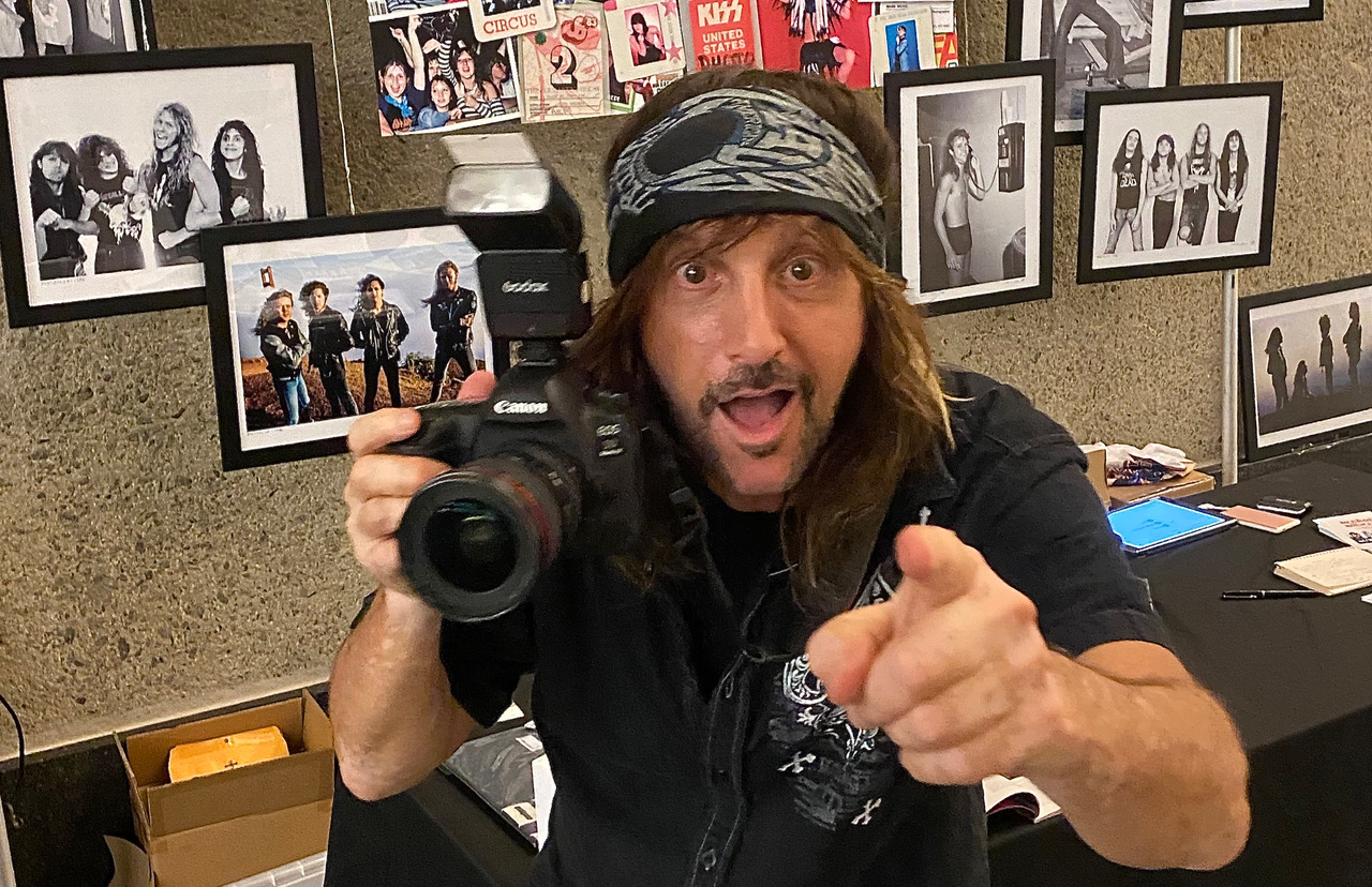 A man holding a camera in front of several pictures.